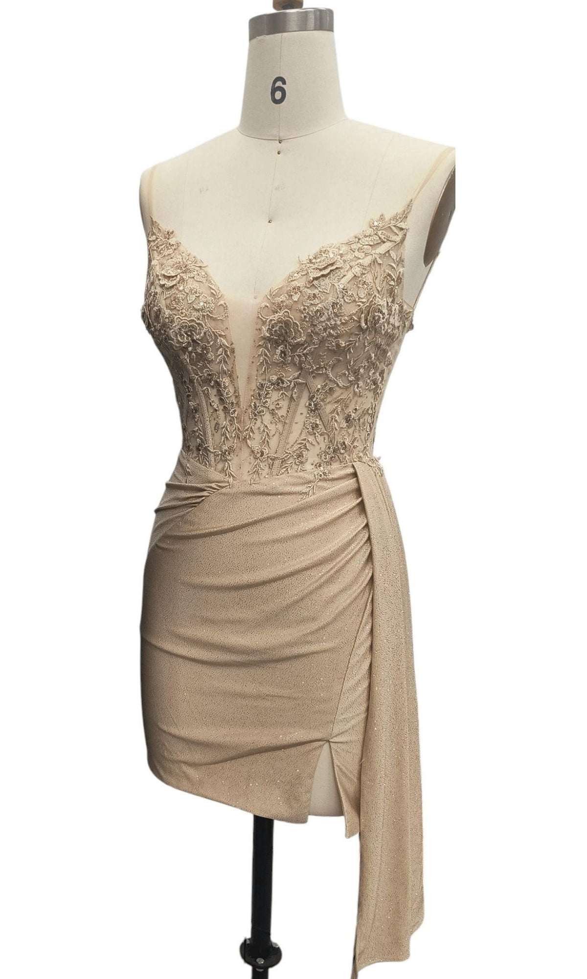 The Side-Drape Short Hoco Dress: 12658 is a sleeveless beige mini dress with a beaded v-neck bodice and draped skirt with side slit, displayed on a mannequin—perfect for homecoming.